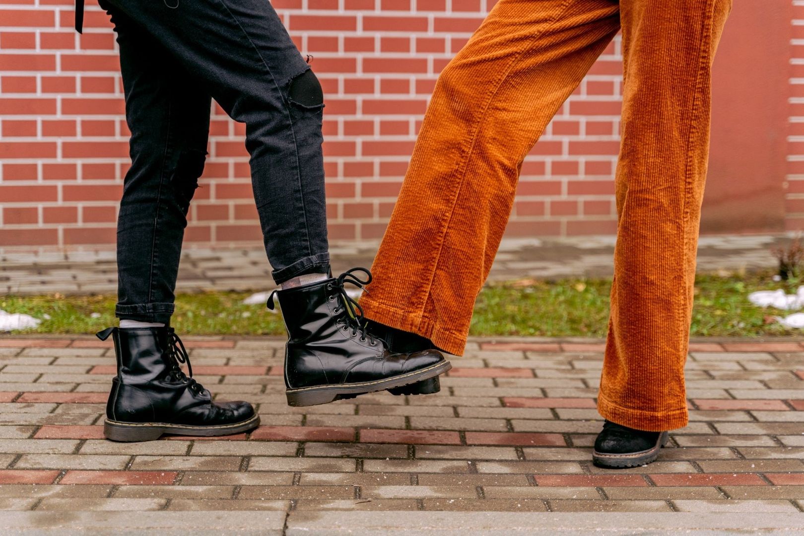 Svarta kängor och orangea byxor på en regn- och slasktålig trottoar