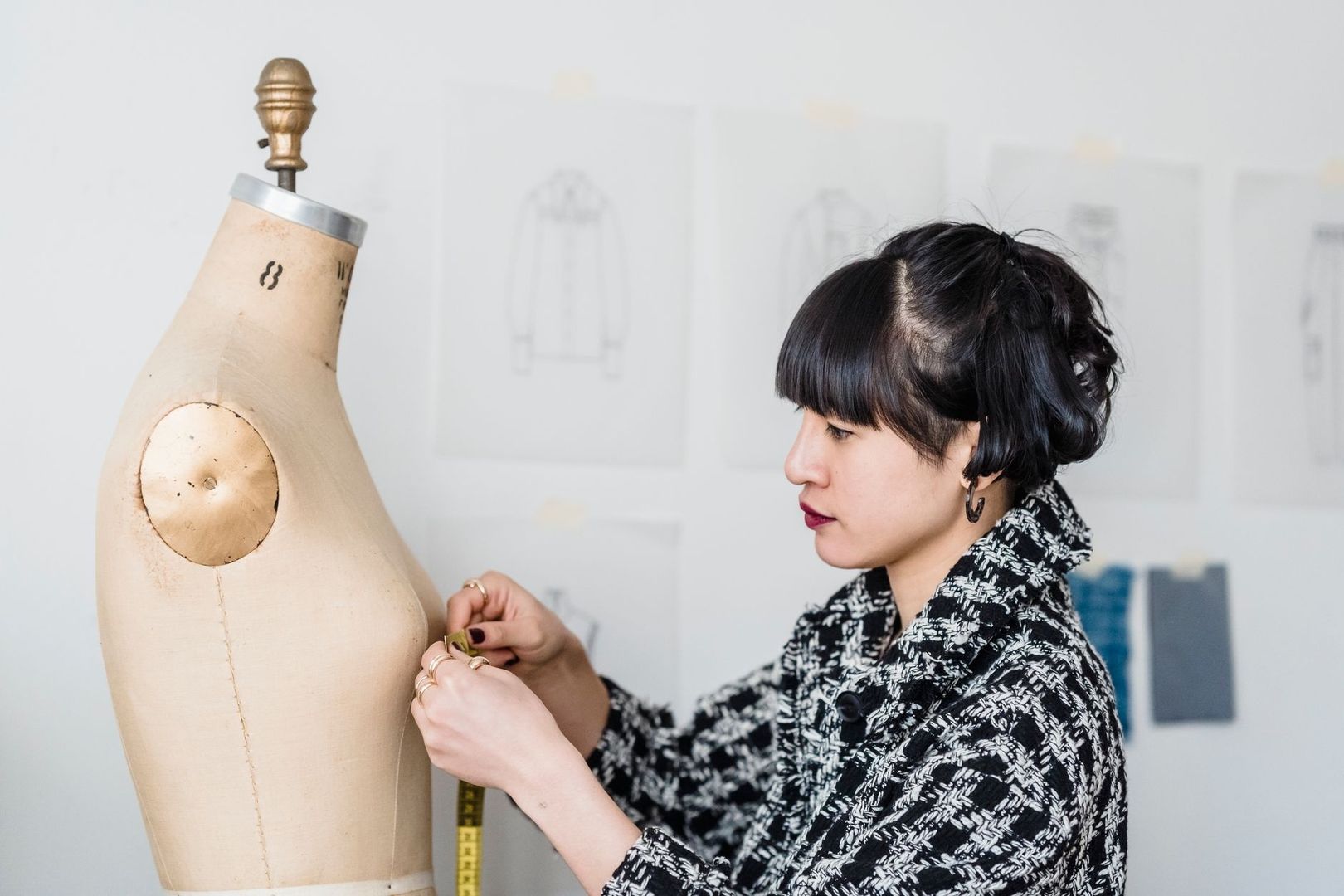 Modedesigner mäter ett tygmönster på en klädprovdocka i ateljén